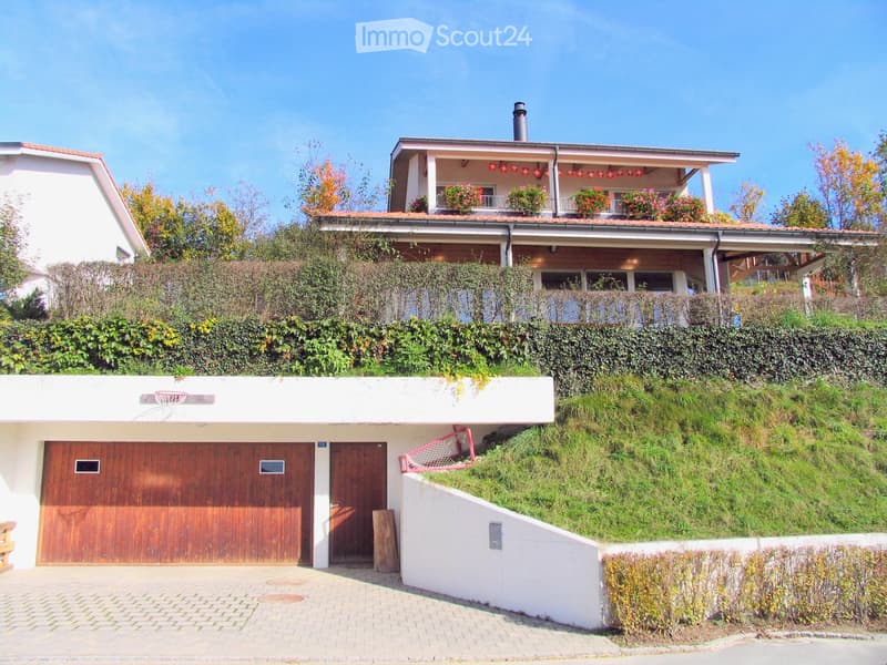 Two-story house with a garage, raised ground floor, and balcony with flower boxes.