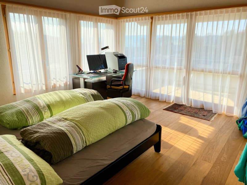 Bright bedroom with a double bed, desk with computer and printer, chair, and large windows with sheer curtains.