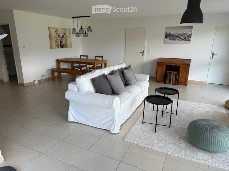 Modern living room with white sofa, grey cushions, coffee table, dining area, and artwork on walls.