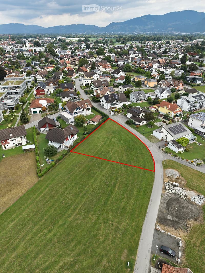 Aerial view of a suburban neighborhood with multiple houses, green lawns, and a highlighted plot of land outlined in red.