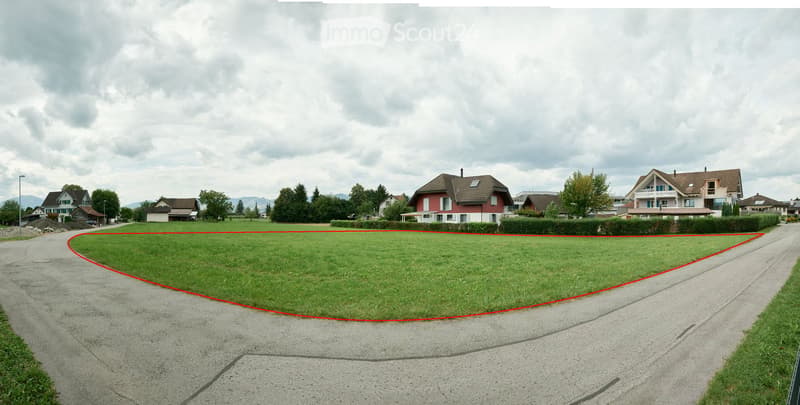 A large, well-maintained lawn area surrounded by residential houses and trees, with a paved driveway running alongside.