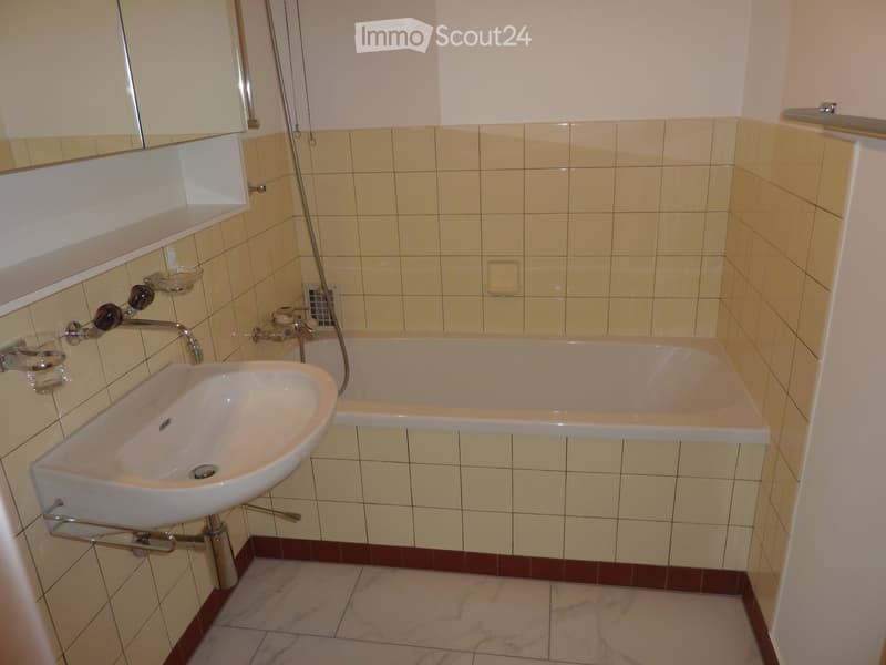 Bathroom with a white sink, bathtub, mirror, and tiled walls.