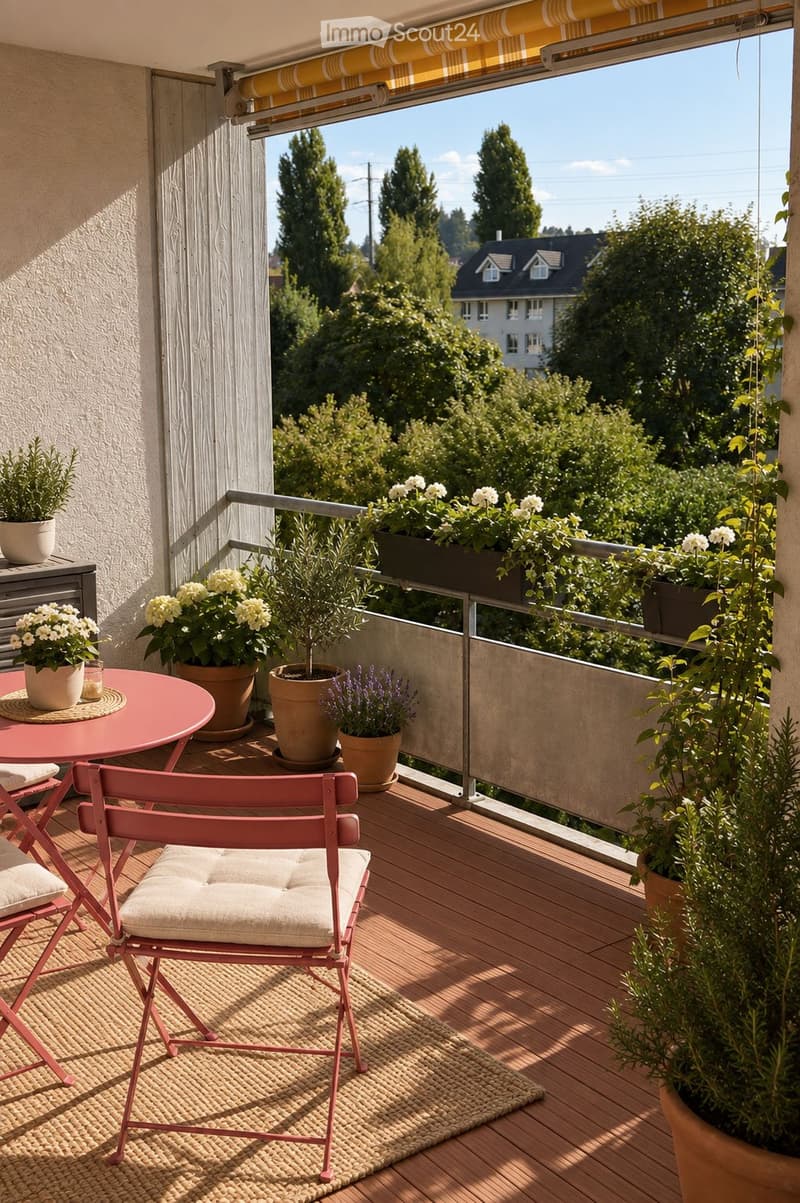 Balcony with wooden decking, pink table and chairs, potted plants, and a view of greenery and houses.