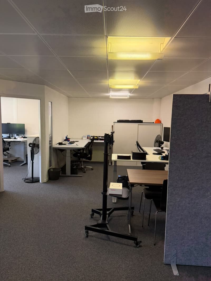 Office space with multiple desks, chairs, computers, fans, and a small table with chairs.