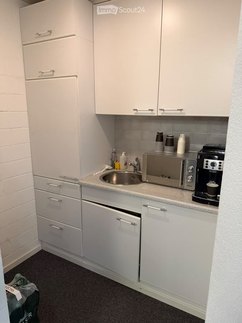 Compact kitchen with white cabinets, a stainless steel sink, microwave, coffee maker, and several cups on the counter.