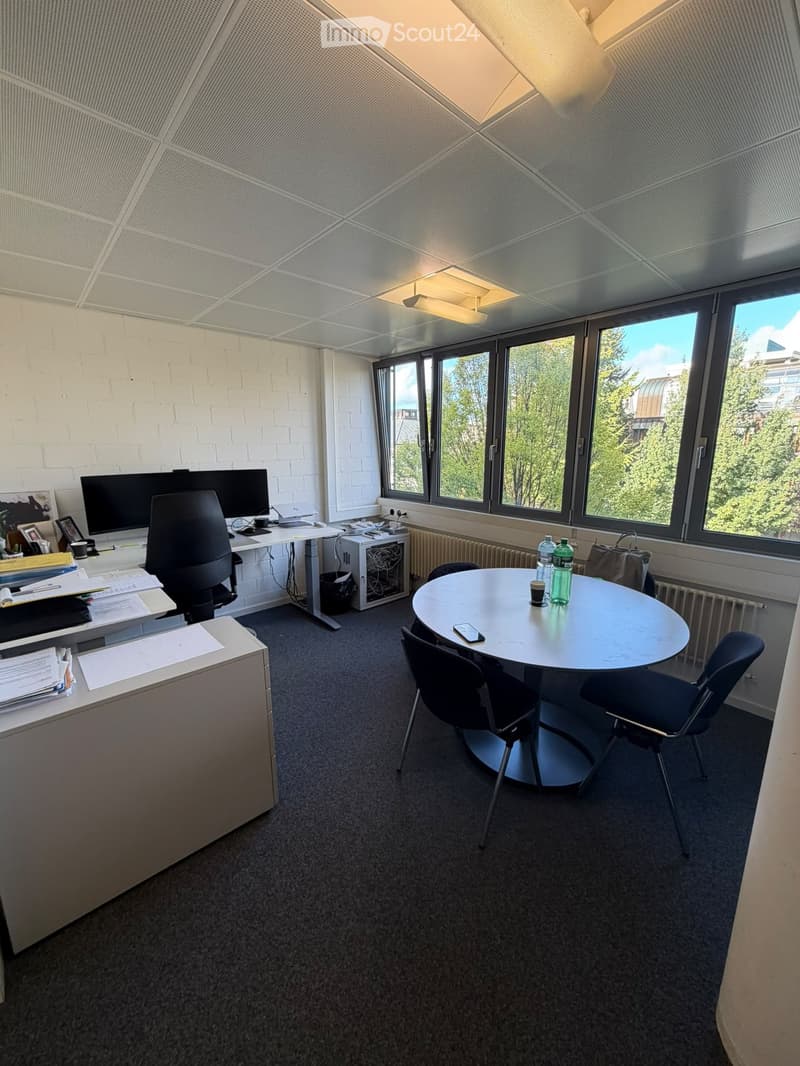 Office space with a round meeting table, chairs, a desk with a computer screen, and various office supplies.