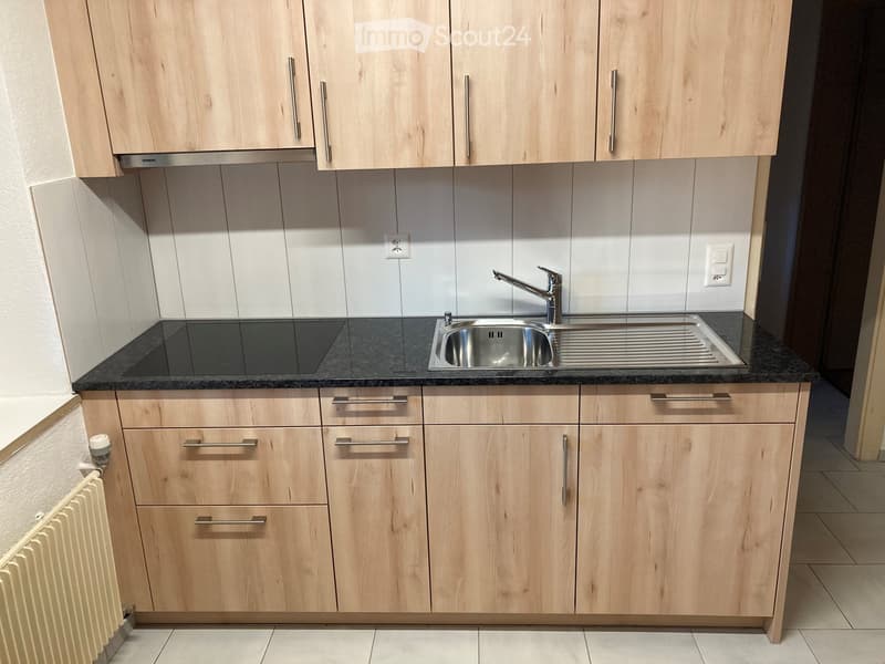 modern kitchen with wooden cabinets, granite countertop, stainless steel sink, faucet, electrical outlet, and a white radiator