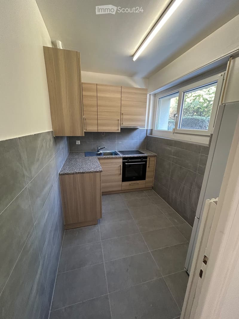 Modern kitchen with wooden cabinets, granite countertop, sink, and built-in oven. Grey tiled walls and floor.