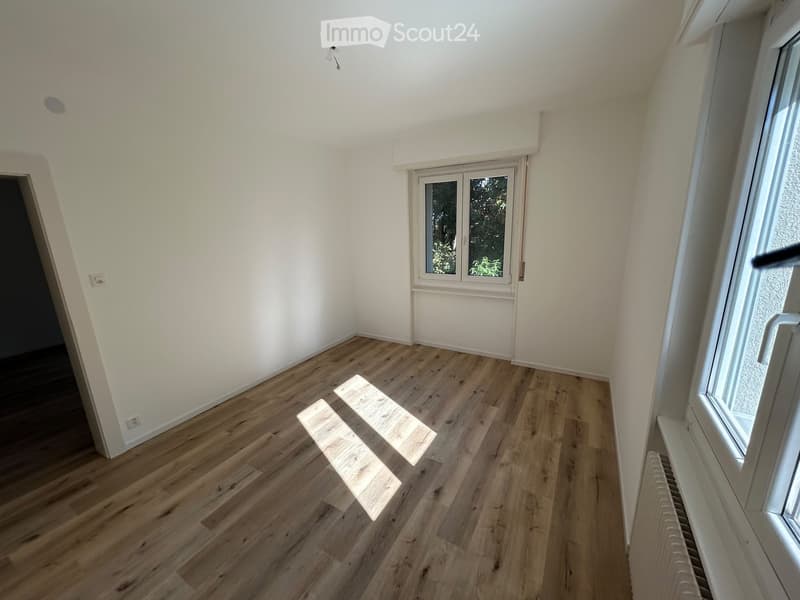 Empty room with light wooden flooring, white walls, and large windows allowing natural light. No furniture or equipment is present.