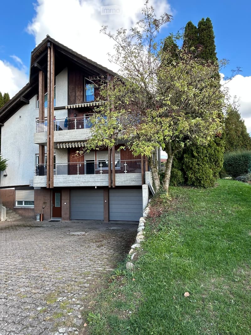 Two-story house with a garage, balcony, and surrounding greenery.