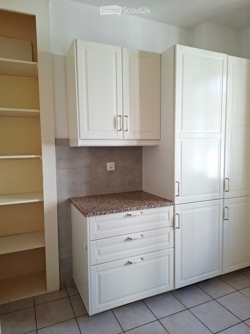 White kitchen with granite countertop, multiple cabinets, and a refrigerator. The cabinets have silver handles and the countertop is speckled with a granite pattern.