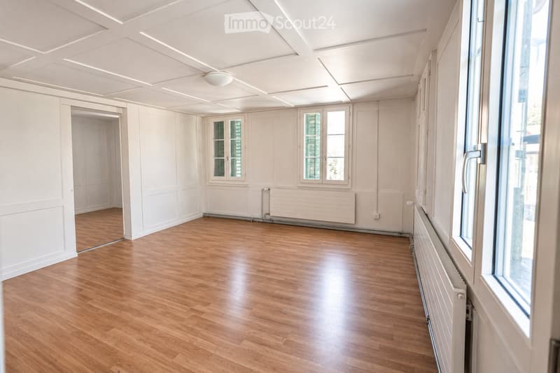 Empty room with wooden flooring, white walls, and large windows. No furniture or equipment present.