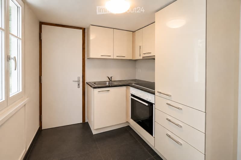Modern kitchen with white cabinets, stainless steel sink, and built-in oven. Features a dark tiled floor and a window on the left side.