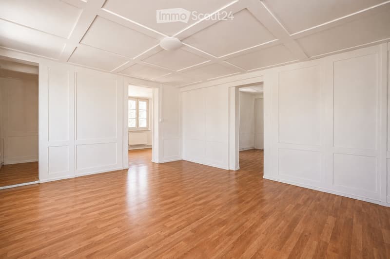 Empty room with white walls, wooden floor, and large windows. No furniture or equipment visible.