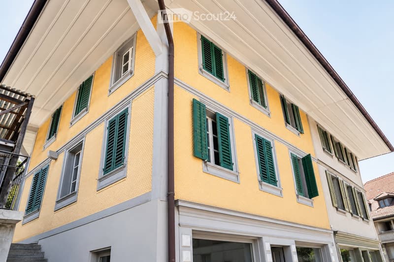 A multi-story residential building with yellow walls, green shutters, and white trim around the windows and roofline.