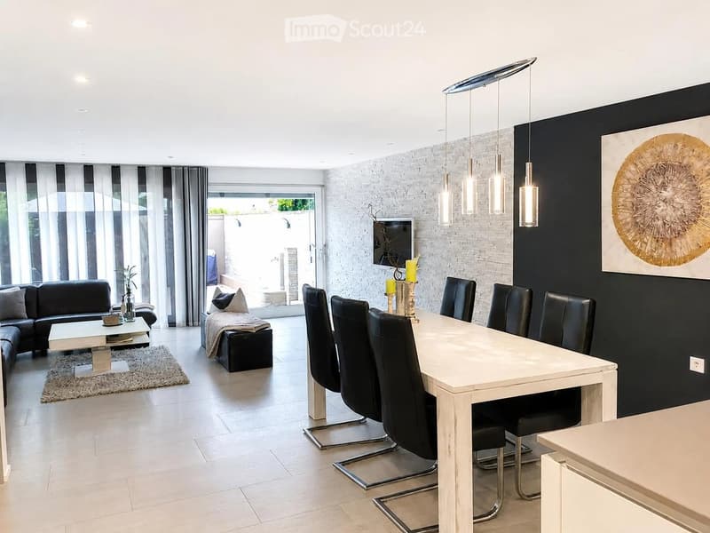 Modern open-plan living and dining area with white dining table, black chairs, sofa, coffee table, ottoman, and large pendant lights.