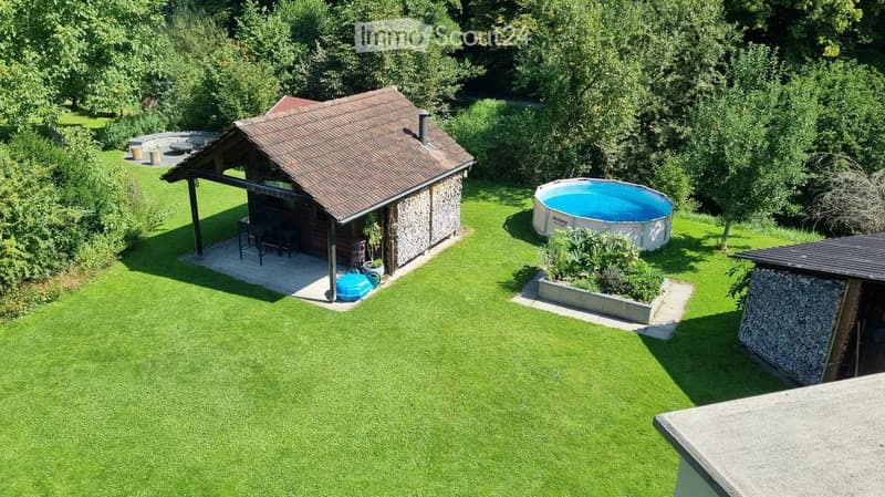 Well-maintained garden with a swimming pool, a small wooden structure with seating, and a stone barbecue area.
