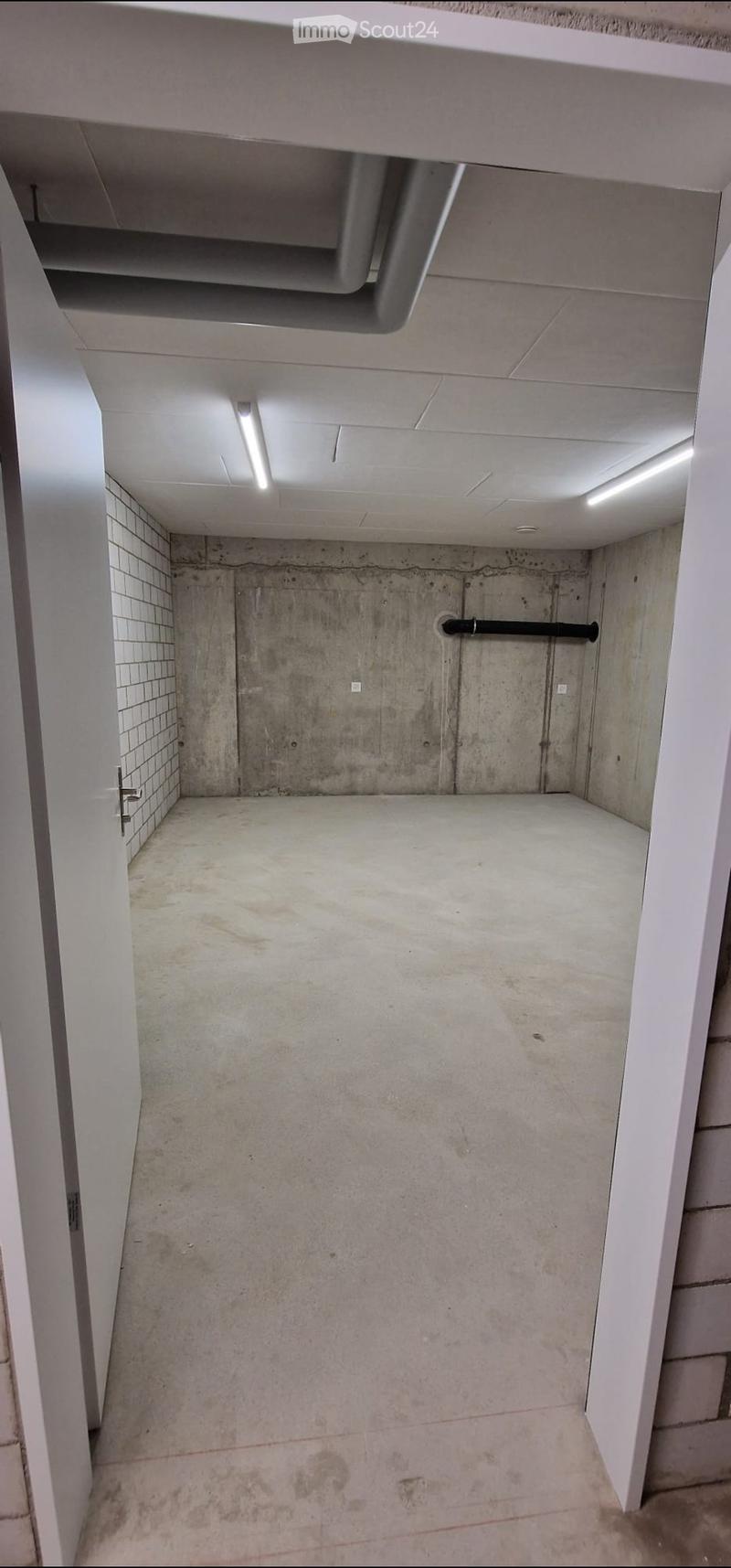 Empty concrete corridor with white tiled walls, exposed pipes, and fluorescent lighting.