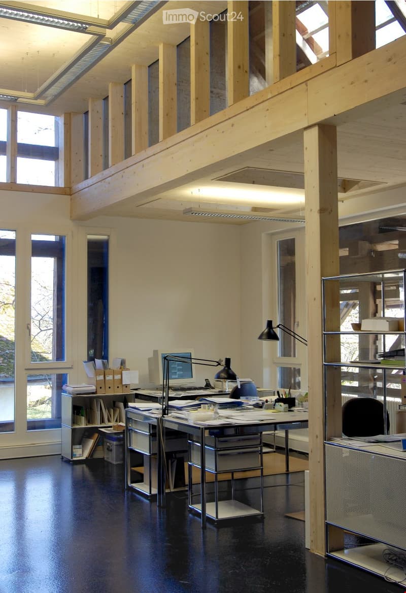 Modern office space with wooden beams, large windows, desks, chairs, lamps, and shelves.