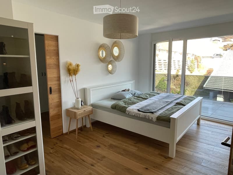 Modern bedroom with a white wooden bed, nightstand, pendant light, and large window with a view.