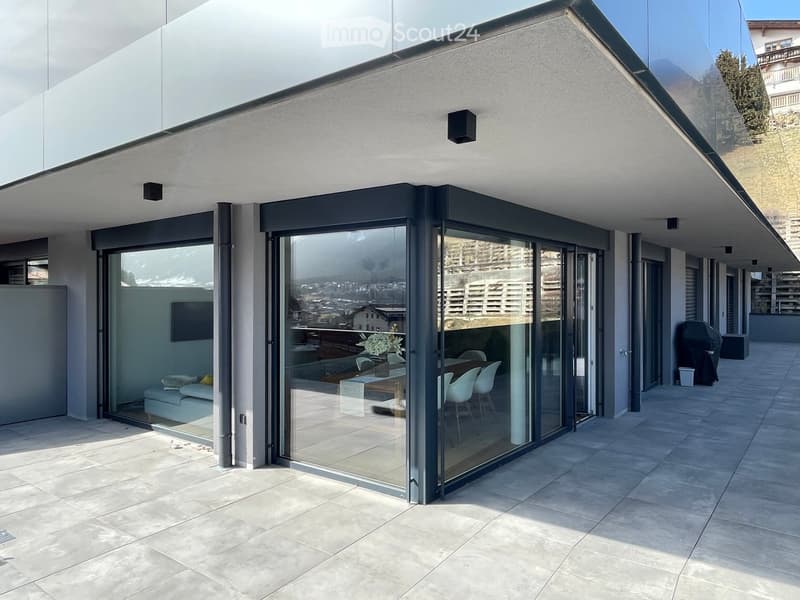 Modern balcony with large glass sliding doors, tiled floor, and a view of the city and mountains.