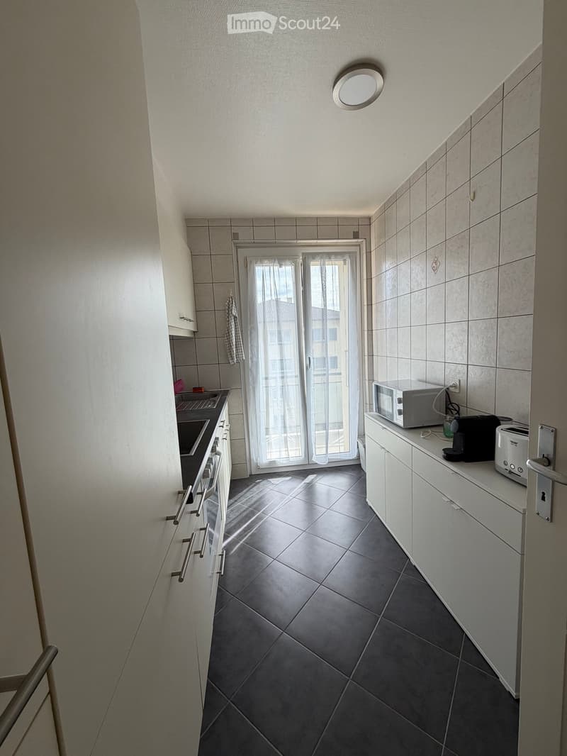 Modern kitchen with white cabinets, dark tiled floor, microwave, toaster, and oven. Features a sliding glass door leading outside.