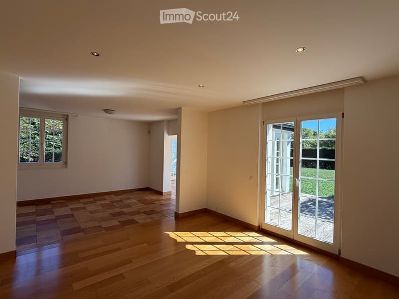 Empty room with wooden flooring, large windows, and sliding glass doors leading to an outdoor area.