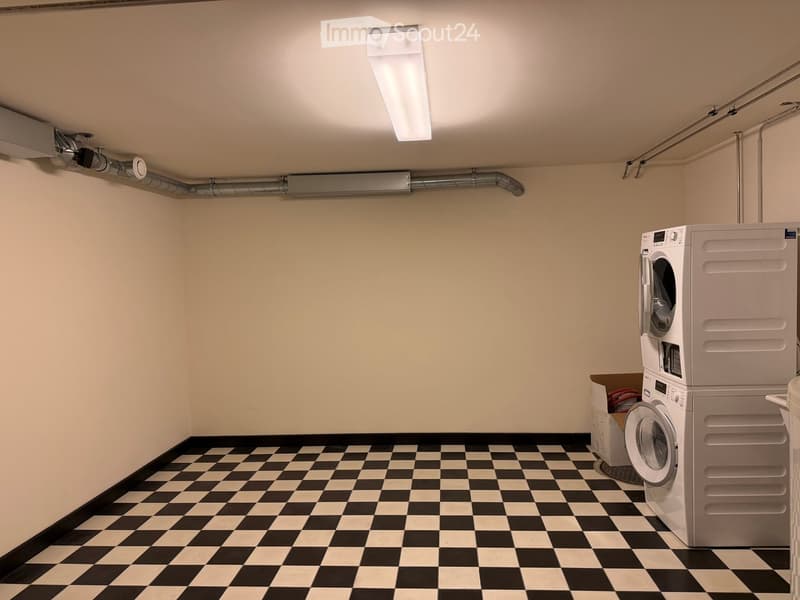 Clean, well-lit laundry room with black and white checkered flooring, white walls, and a stacked washer and dryer unit.