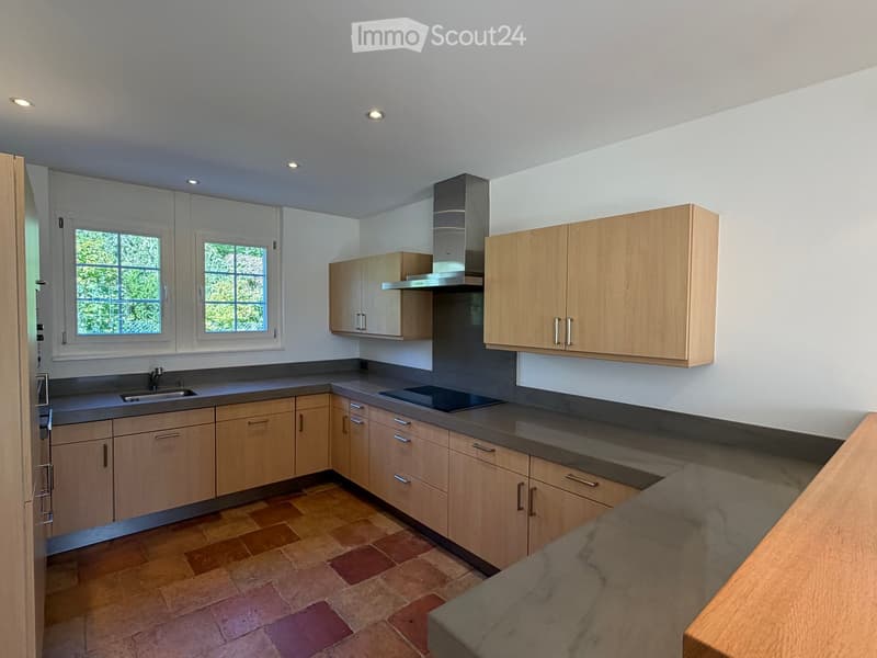 Modern kitchen with light wooden cabinets, stainless steel appliances, and a tiled floor.