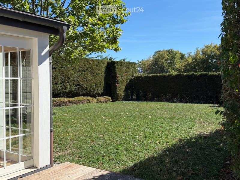 A well-maintained garden with a wooden deck, neatly trimmed hedges, and a clear view of the house exterior.