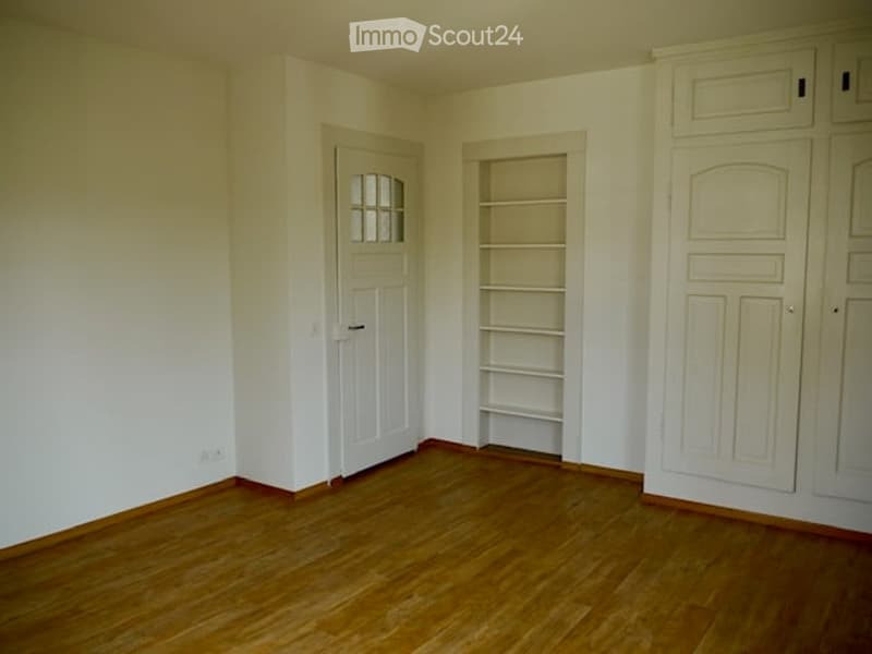 Empty room with wooden flooring, white walls, a built-in shelf unit, and a door with a glass panel.