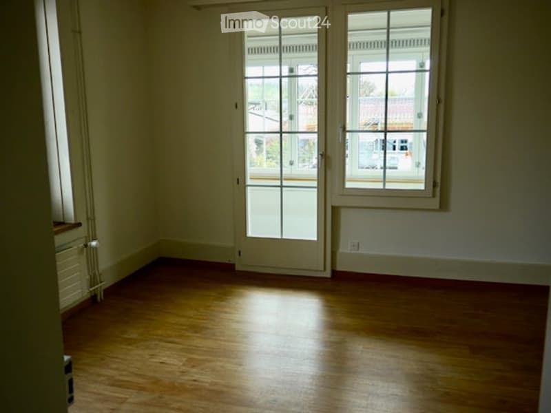 Empty room with wooden flooring, large windows, and a door leading outside. No furniture or equipment present.