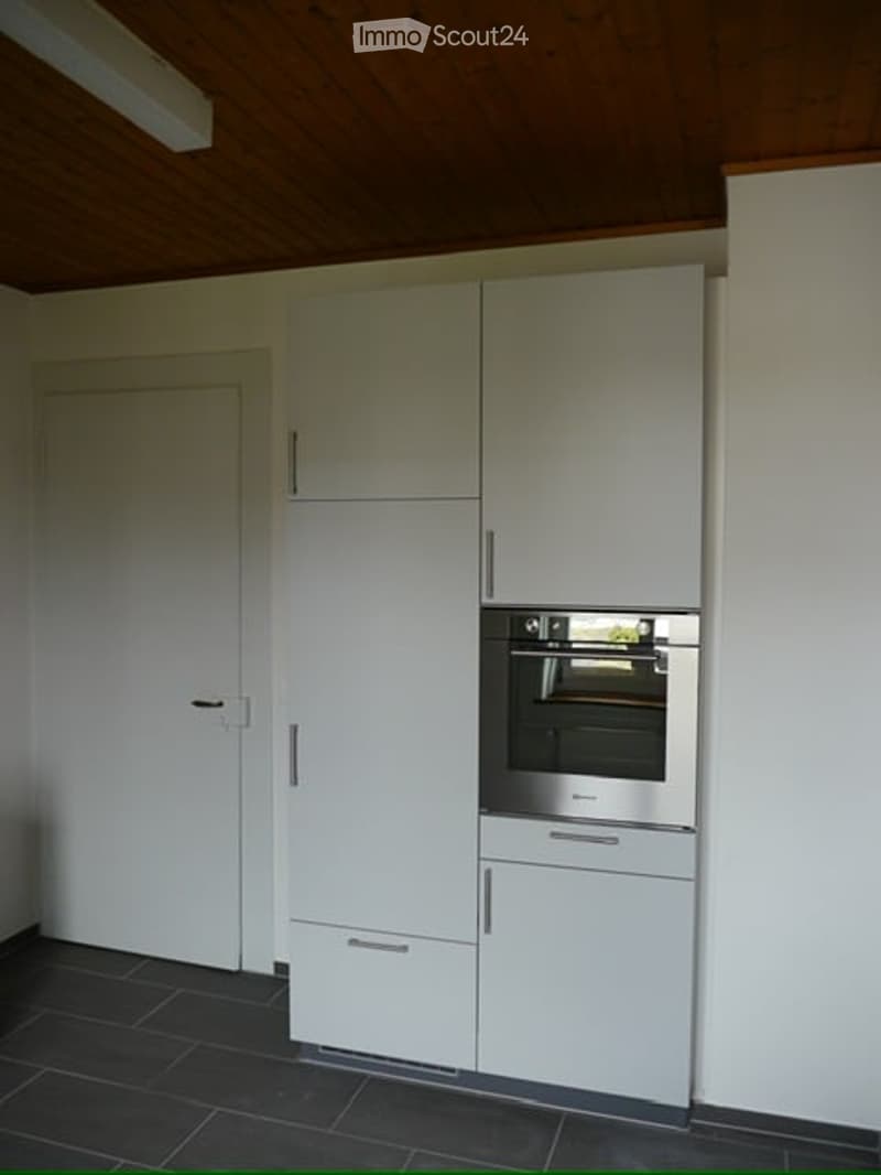Modern kitchen with white cabinets, stainless steel oven, dark tiled floor, and wooden ceiling.