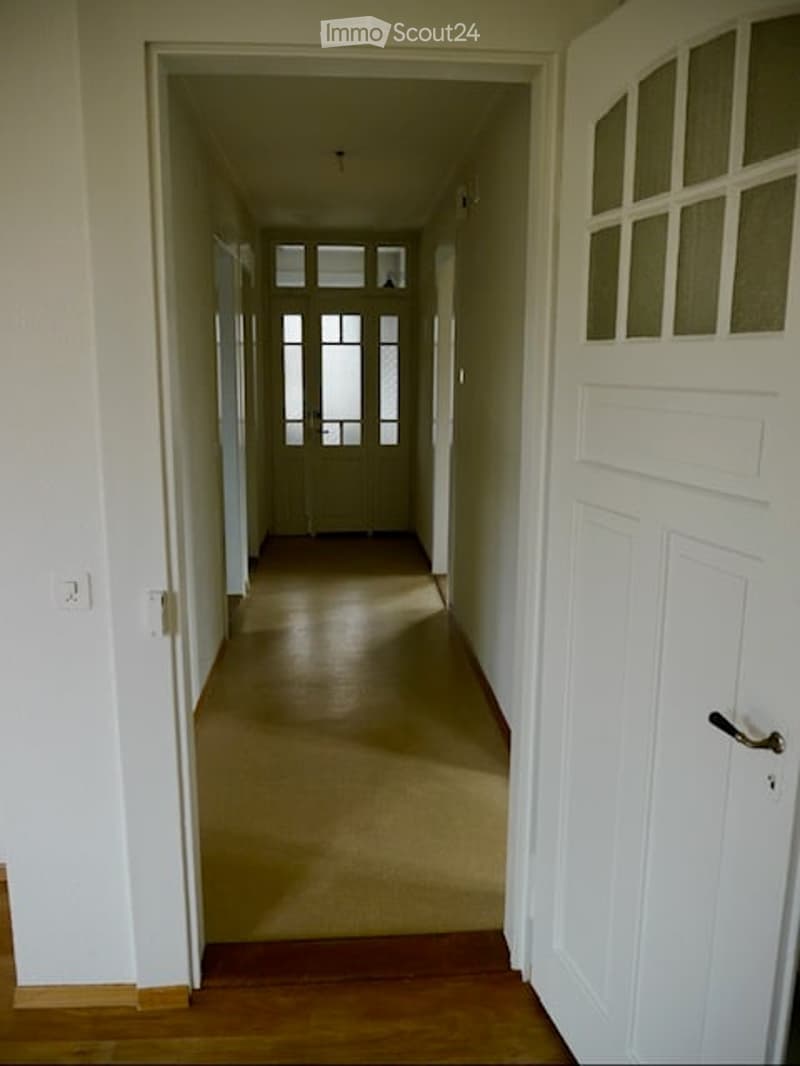 Empty hallway with light-colored walls, carpeted floor, and white doors on both sides.