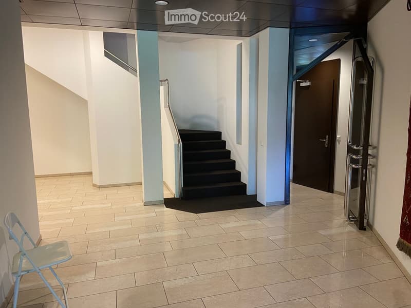 Empty hallway with tiled floor, white walls, a staircase with black steps, and a closed door on the right side.