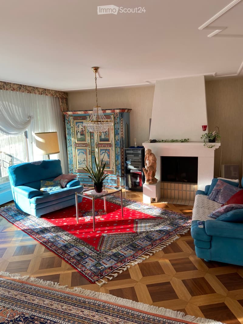 Living room with wooden flooring, fireplace, two blue sofas, coffee table, chandelier, and decorative items.