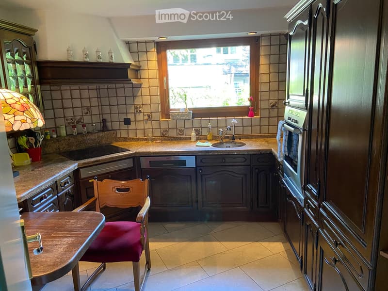 Well-lit kitchen with wooden cabinets, granite countertops, a sink, oven, refrigerator, and a small dining area with a table and chair.