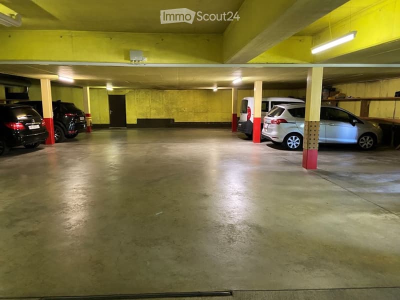 Underground parking area with several parked cars, concrete floor, yellow walls, and fluorescent lighting.