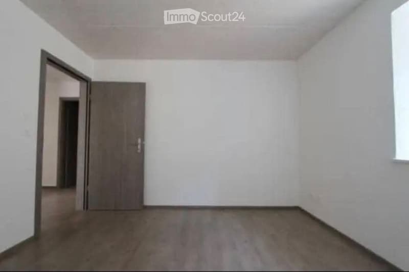 Empty room with white walls, wooden floor, and a single door leading to another space.