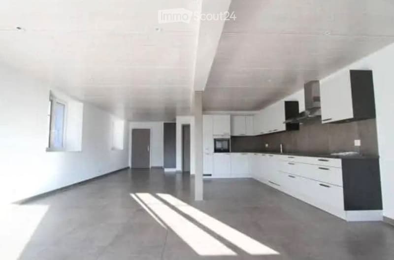 Modern kitchen with white cabinets, dark countertops, and stainless steel appliances. The space is open and well-lit with natural light coming through a window on the left side.