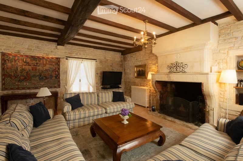 Cozy living room with exposed wooden beams, stone walls, fireplace, striped sofa, coffee table with flower arrangement, television, and lamps.
