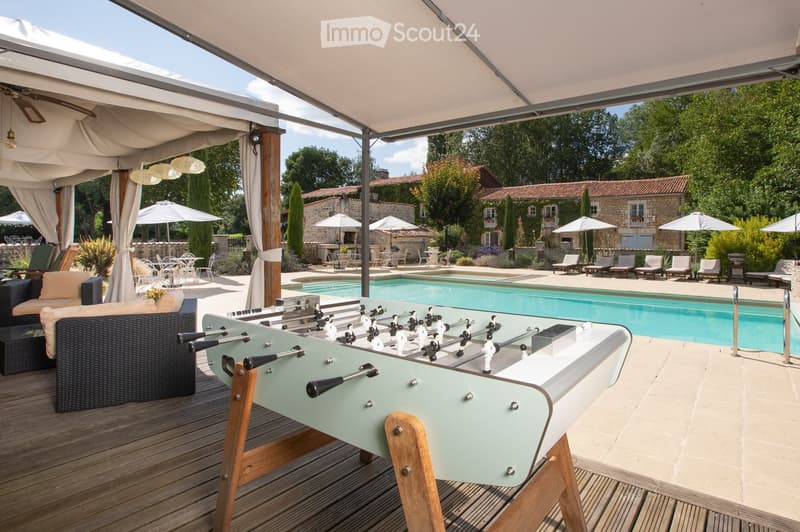 Outdoor area with a swimming pool, covered seating area, foosball table, lounge chairs, and umbrellas.