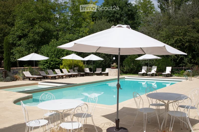 A spacious outdoor area featuring a swimming pool surrounded by lounge chairs, umbrellas, and a dining set with a table and chairs.