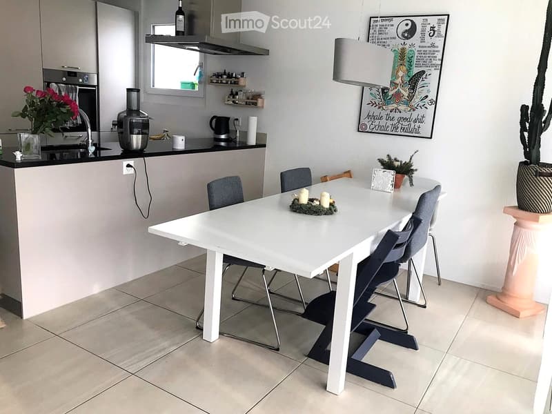 Modern kitchen with a white dining table and chairs, a sink with a faucet, an oven, a blender, and decorative items including a cactus and a flower arrangement.