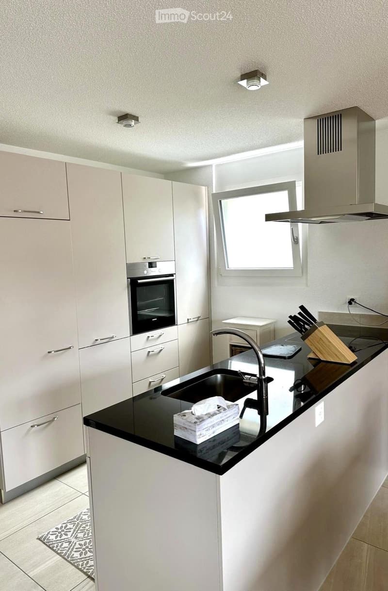 Modern kitchen with white cabinets, black countertop, stainless steel sink, and built-in oven. Features a knife block and tissue box on the counter.