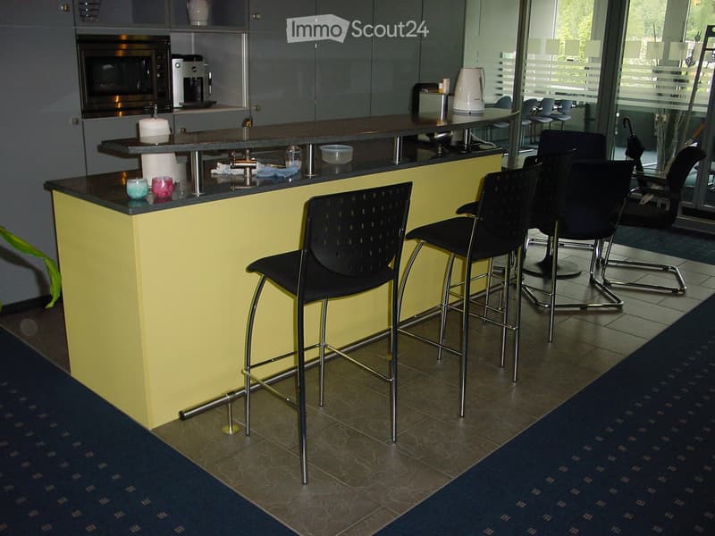 Brightly lit room with a yellow bar counter, several black stool chairs, microwave, coffee maker, and a Keurig machine on the counter.