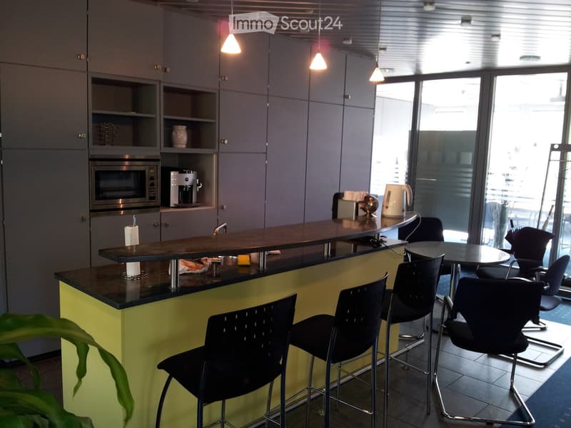 Modern kitchen with grey cabinets, a central island with a dark countertop, and various appliances including a microwave and coffee maker. Bar stools and chairs are arranged around the island and a small table.