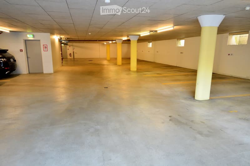 Empty underground parking area with concrete floors, yellow support columns, and a parked car visible in the background.
