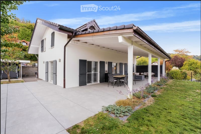 Modern two-story house with white exterior, dark shutters, and a covered patio area with outdoor furniture.