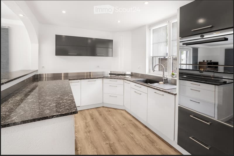 Modern kitchen with white and black cabinets, granite countertop, stainless steel sink, and built-in oven.